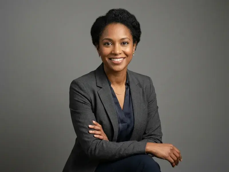 Portrait professionnel de studio d'une femme en reconversion, souriante et confiante, vêtue d'une chemise élégante, sur fond neutre. Éclairage doux et professionnel.