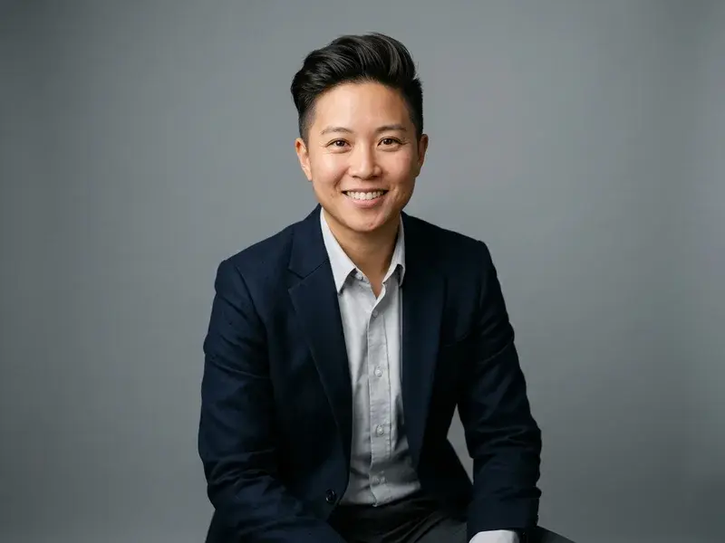 Portrait professionnel d'une personne confiante, en tenue d'affaires, regardant l'objectif avec un léger sourire, sur fond neutre et éclairage studio doux.
